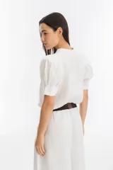 Pantalón blanco de lino, corte palazzo, tiro medio-alto, con tablas delanteras, elástico en la parte trasera y bolsillos laterales.