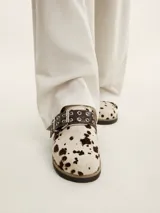 Zueco de cuero vacuno con estampado animal print tipo vaca, con hebilla decorativa metálica con ojales y suela de corcho con vira reforzada.