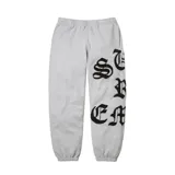 Pantalón de jogging gris con diseño de letras bordadas en color negro sobre la pierna izquierda. Presenta cintura elástica y puños ajustados en los tobillos.