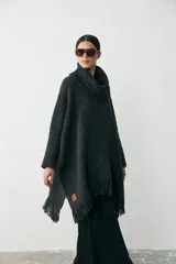 Poncho de tejido artesanal en color negro, con cuello alto tipo polera, mangas largas y terminación con flecos en el ruedo. Presenta una etiqueta de cuero decorativa en la parte inferior.