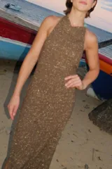 Vestido midi de tejido de punto con acabado brillante, diseño halter con espalda descubierta y detalle de piedras de resina en el cuello. Presenta un tajo lateral pronunciado.