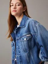 Campera de denim azul medio vintage, corte relaxed boxy, confeccionada con 20% de algodón reciclado. Tiene cuello en punta, bolsillos de parche en el pecho, bolsillos de hendidura en la cintura, botones metálicos de la marca y parche con logo de Calvin Klein en el bolsillo del pecho.