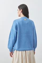 Sweater de tejido liviano con silueta relajada, hombros caídos y mangas largas con puños ajustados. Presenta cuello redondo y lazos ajustables en el bajo.