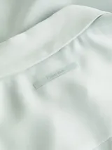 Camisa celeste de crepé de china reciclado, de corte holgado, con cuello en punta, cierre de botones, hombros caídos y puños con botones.