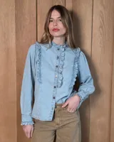Camisa de denim celeste con cuello alto con volados, botonadura frontal y detalles de volados verticales a lo largo del frente. Cuenta con mangas largas abullonadas y puños con volados.