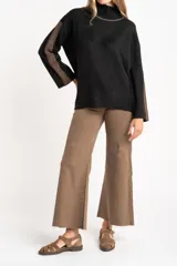 Polera de punto con calce oversize, cuello alto y mangas largas. Presenta un diseño en color negro con franjas laterales en las mangas y detalle en el cuello en tono bronce con acabado brillante.