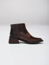 Botinetas de caña baja confeccionadas en una combinación de cuero napa y gamuza en tono bordó. Presentan un diseño de paneles con una banda central horizontal, puntera cuadrada y taco geométrico de color negro.