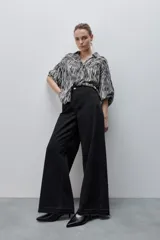 Jean wide leg negro de tiro alto, confeccionado en denim rígido, con diseño de cinco bolsillos, presillas para cinto, cierre frontal con botón y ruedo desflecado.