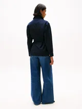 Campera azul marino estilo militar con cuello inglés, cierre de botones dorados con el escudo TH en relieve, cinturón anudable, cuatro bolsillos delanteros con botón, puños con botón y logo metálico de Tommy Hilfiger en el puño.