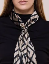 Pañuelo satinado Jessica Mc Clintock con diseño geométrico en tonos negro y beige. Incluye un broche metálico circular con aplique central para ajustar el drapeado.
