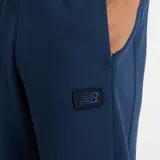 Pantalón deportivo New Balance modelo Track Pant, color azul marino, de corte ancho y holgado, con cordón ajustable en la cintura y un pequeño parche con logo en el muslo.