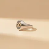 Anillo tipo sello de plata 925 con aplique central de figuras de niños en oro 18k sobre fondo texturizado oscuro.