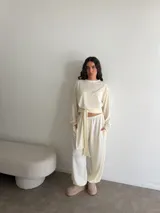 Conjunto de dos piezas color marfil, compuesto por una remera de manga larga con lazo ajustable en la cintura y un pantalón holgado de corte relajado con elástico en la cintura y bolsillos.