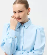 Camisa de crepé color blanco, con cuello inglés, manga larga abullonada con puños abotonados y cierre frontal oculto con botón diferenciado en el cuello.