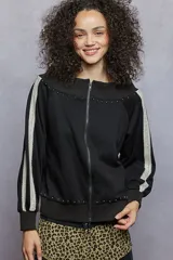 Campera negra con diseño strapless, cierre frontal completo y mangas largas con detalle de franjas laterales de encaje. Presenta apliques de tachas metálicas en el cuello y en el ruedo.