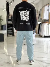 Buzo oversize color beige, con diseño gráfico en la espalda con el texto 'Warm Vibes' en tono marrón y tipografía psicodélica, acompañado de frases secundarias.