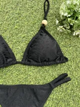Bikini negra con corpiño triangular que tiene un aplique de piedra en el bretel y bombacha colaless con tiras ajustables laterales.