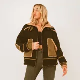 Campera gamulán de diseño oversize en color verde oscuro con detalles en corderito beige, bolsillos frontales grandes, cierre de cremallera y cuello solapa.