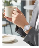 Reloj de pulsera analógico para mujer con caja de metal plateado, bisel decorado con cristales y malla de acero inoxidable. Esfera con fondo nacarado y marcadores de hora con cristales.