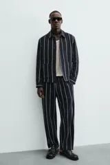 Pantalón de corte relajado, color azul marino, con rayas verticales blancas finas. Presenta cintura elástica ajustable con cordón interior y bolsillos laterales y traseros de plastrón.