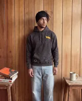 Canguro con capucha de corte regular, color negro con efecto lavado. Presenta un diseño gráfico estampado en la espalda en color naranja que incluye ilustraciones de carpinchos sobre una cuadrícula de globo terráqueo y texto descriptivo.