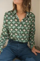 Camisa de manga larga con cuello camisero y cierre frontal de botones, confeccionada en tela estampada con un patrón geométrico de abanicos en tonos verdes y beige.