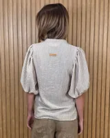 Camisa de algodón a rayas color beige y blanco, con escote en V, cuello mao y mangas cortas abullonadas. Cuenta con cierre frontal de botones oscuros.