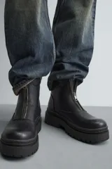 Bota de caña media con cierre frontal mediante cremallera, confeccionada en material con textura. Presenta una horma redonda y una suela de plataforma con diseño track.