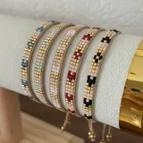 Pulsera artesanal confeccionada con cuentas Miyuki en tonos beige, dorado y detalles en rojo, con diseño ajustable.