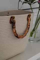 Bolso de mano de cuerda color crema con asas de bambú y detalles de cuero marrón.