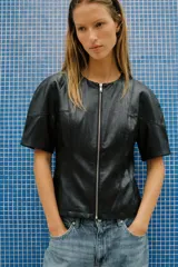 Cuerpo crop efecto piel de color negro, con cuello redondo y manga corta. Presenta costuras marcadas y cierre frontal con cremallera metálica.
