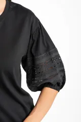 Remera negra de algodón con mangas cortas abullonadas que presentan detalles de encaje bordado y calado en los extremos.