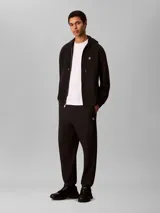 Jogger de felpa Calvin Klein color negro, con cintura elástica, bolsillos laterales y puños acanalados en los tobillos. Presenta el monograma de la marca bordado discretamente en la pierna.