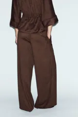 Pantalón de tiro alto con diseño de pierna ancha, confeccionado en tejido con efecto ante. Cuenta con cintura elástica y bolsillos laterales ocultos en la costura.