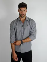 Camisa de manga larga con estampado de rayas verticales finas en tonos gris y blanco. Presenta cuello clásico, cierre frontal con botones y un pequeño logo bordado en el pecho.