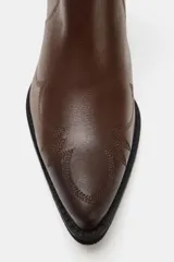 Botín cowboy de piel color marrón con detalles bordados en el cuerpo, elástico lateral, tirador trasero y tacón ancho en bloque con acabado en punta.
