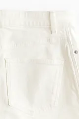 Short pollera de cinco bolsillos en denim de algodón color blanco, con diseño de tiro alto, cierre frontal y botón metálico.