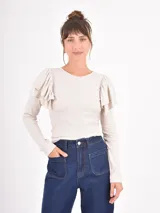 Remera de manga larga en color beige, confeccionada en tejido acanalado, con cuello redondo y detalle de volados en los hombros.