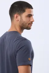 Remera de manga corta color azul oscuro, con cuello redondo y detalle de bordado pequeño en el centro del pecho que representa tres figuras geométricas con forma de árboles y el texto Legacy Brand.