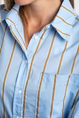 Camisa de corte oversize con estampado de rayas verticales en tonos azul y beige. Presenta cuello camisero clásico, cierre frontal con botones, bolsillo en el pecho y mangas largas con puños rectos.