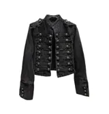 Chaqueta corta de denim negro con diseño de inspiración militar, cuello mao, cierre frontal con múltiples botones metálicos y detalles de trenzado horizontal. Presenta charreteras en los hombros y puños con botones decorativos.