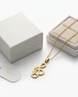 Dije con forma de clave de sol, elaborado en acero con baño dorado, con textura punteada en su superficie.