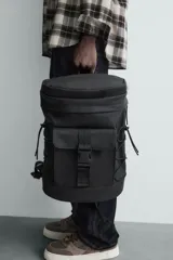 Mochila negra con acabado engomado, compartimento principal con cierre de cremallera, bolsillo interior con cremallera, bolsillo frontal con hebilla de liberación rápida, parte posterior acolchada, asa de mano y dos asas de hombro ajustables.