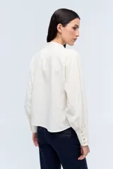 Camisa color crema a rayas verticales finas, con cuello mao con lazos para atar, escote en V y mangas largas con puños abotonados.