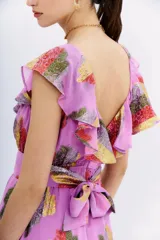 Vestido midi sin mangas, color lila, con escote en V adornado con volados y cinturón a tono. Presenta un estampado floral en jacquard de lurex multicolor con tonos rojos, amarillos y plateados.