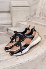 Championes urbanos de diseño tricolor, combinando paneles de cuero en tono caramelo, gamuza beige y detalles en charol negro. Presentan cordones negros, suela blanca con base dentada en color caramelo y tirador en el talón.