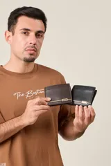 Billetera de cuero sintético con acabado liso, diseño plegable y detalle metálico decorativo en la parte frontal.