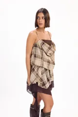 Vestido corto sin mangas con tirantes finos, diseño en capas con superposición drapeada de tela a cuadros tipo tartán en tonos beige y marrón sobre una base de tela marrón lisa.