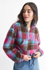 Buzo crop de corderito con estampado a cuadros en blanco, negro y rojo, con cierre de cremallera en el cuello.