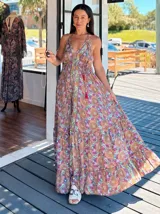 Vestido largo tipo solera, con escote en V y tirantes finos, confeccionado en seda estampada con motivos florales y patrones geométricos en tonos azules, naranjas y morados. Presenta un corte amplio y volados en el ruedo.